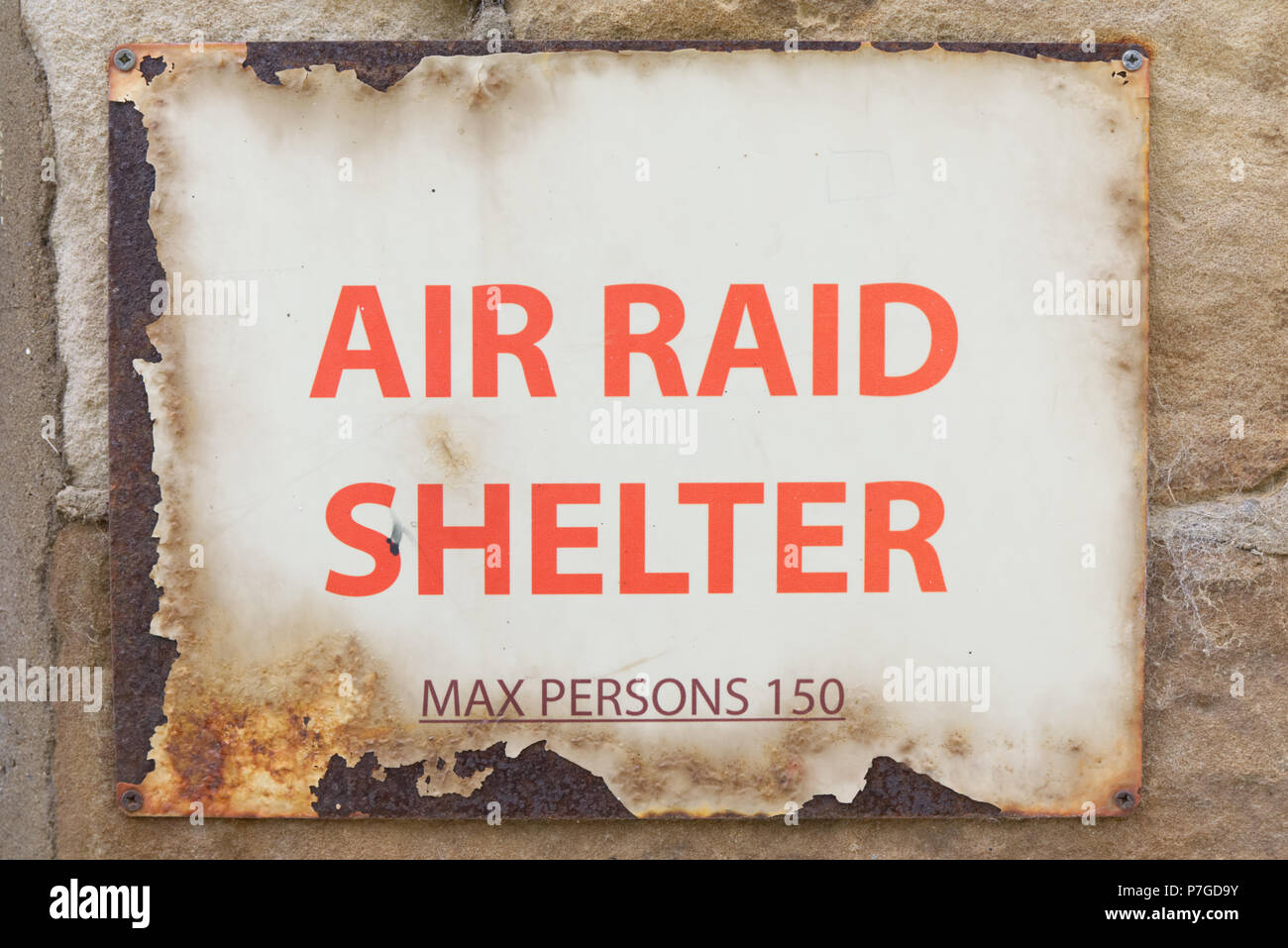 Air Raid Shelter Sign Max Persons 150 decayed old vintage warning sign with red text on rusty metal screwed to wall. World War 2 concept Stock Photo