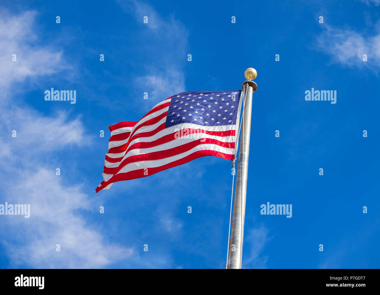 Waving flag of the United States against the blue sky with white clouds ...