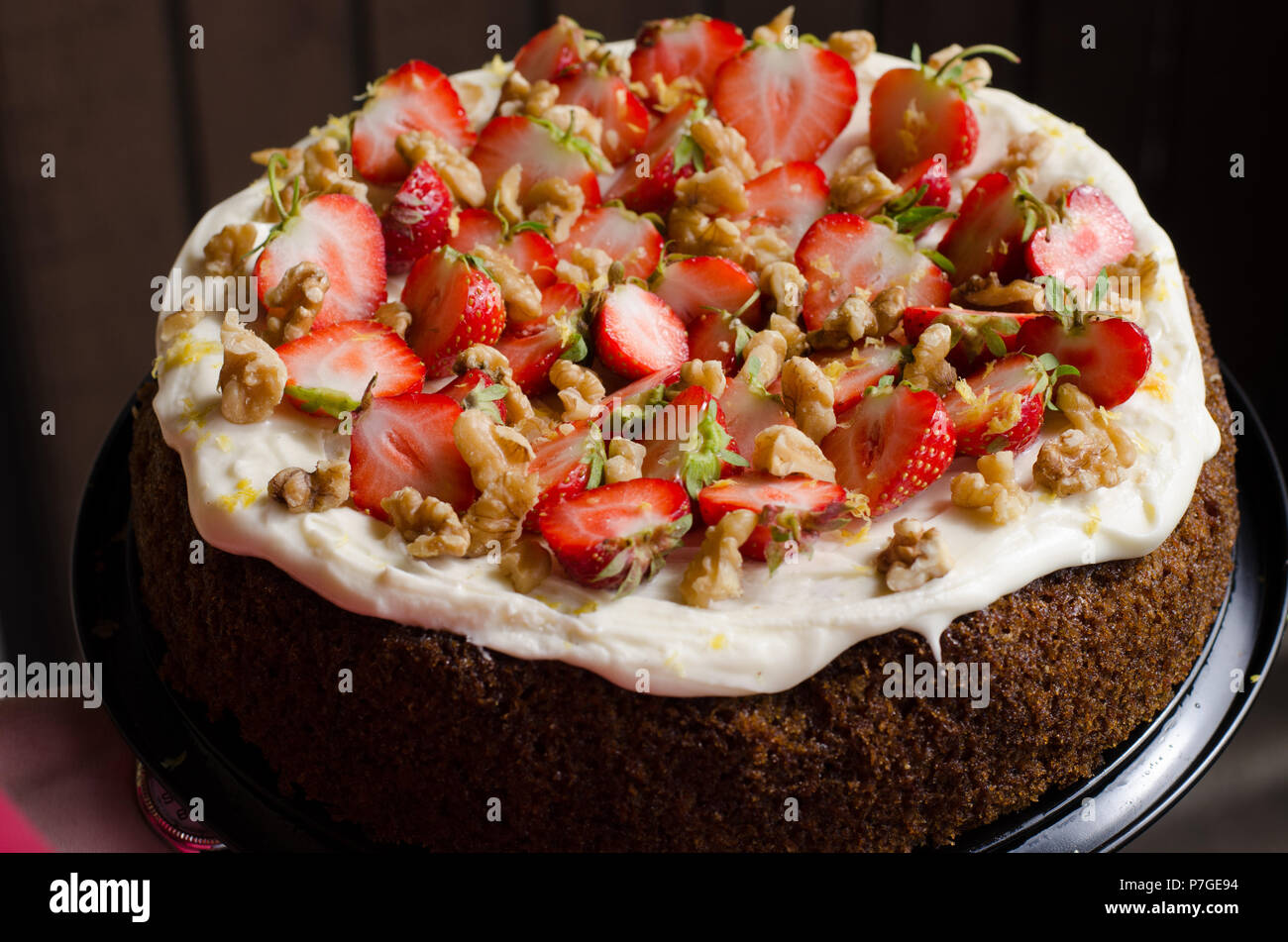 A carrotcake decorated with fresh strawberries and walnuts on top of a frosting of cream cheese, icing sugar and lemon. Stock Photo