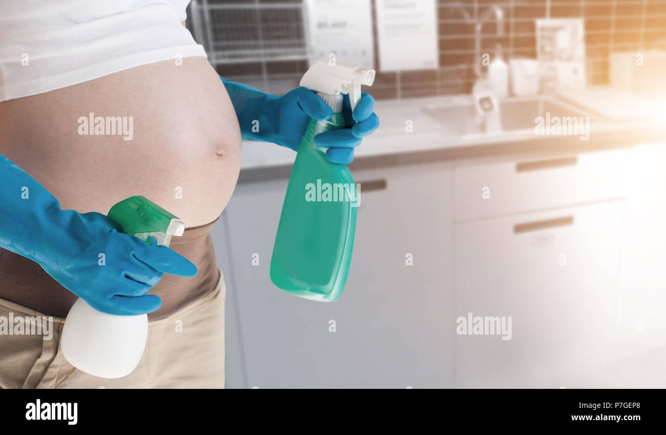 A pregnant woman wearing blue gloves cleaning the toilet Stock Photo