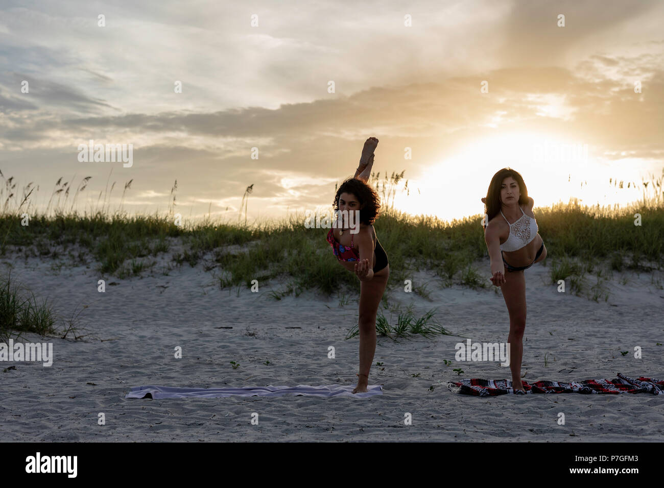 Two women wearing bikinis doing a yoga workout on the beach at sunset
