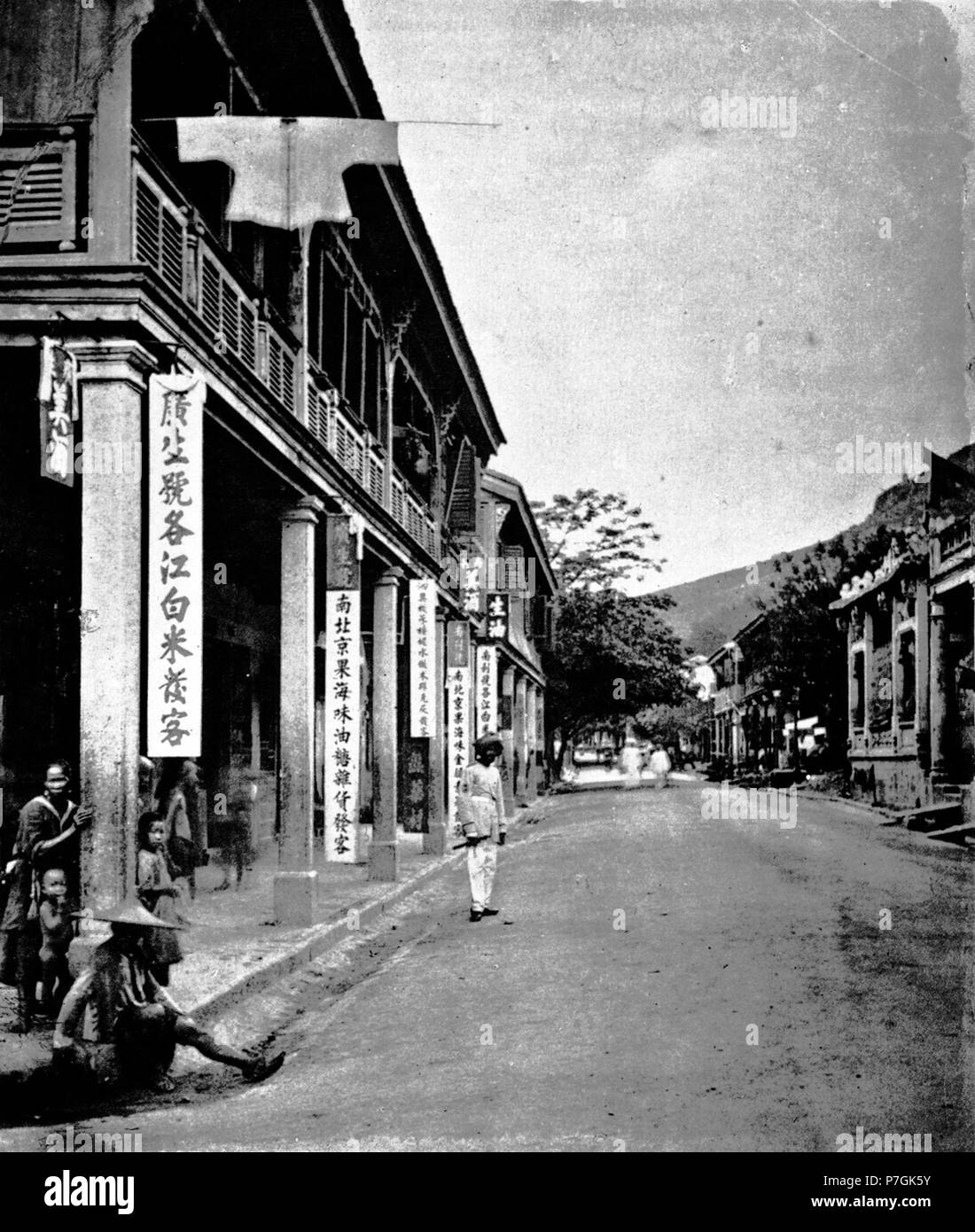 English: John Thomson: IN the street shown in the picture Hong-kong residents will readily recognize the semi-Chinese, semi- European roadway which leads to Wanchi, Wong-nei chong, or Happy Valley. It is chiefly occupied by native shopkeepers, who supply the wants of the soldiers and their families, residing in the extensive barracks of the neighbourhood. Among others, there is a Chinaman who has been some years in California, where he learned the art of foreign shoe-making. He imports the leather from America, and has taught a number of workmen, whom he has in his employ, to make boots and sh Stock Photo