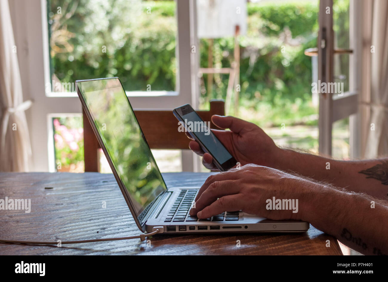 male hands texting on smartphone while working on laptop Stock Photo