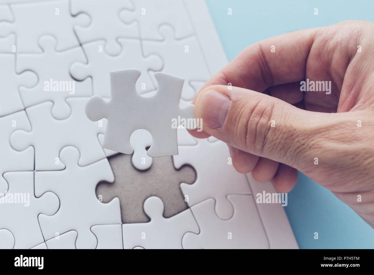 Man successfully solving jigsaw puzzle, hand putting a missing piece to complete the solution Stock Photo