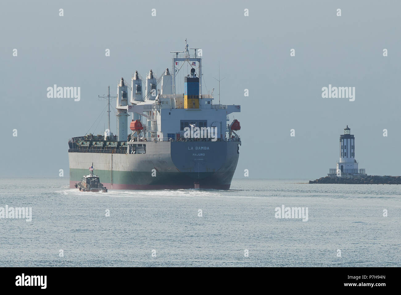 Harbor Pilot Boat Follows The Bulk Carrier, LA BAMBA, Under Way And Leaving The Port Of Los Angeles, California. The Angels Gate Lighthouse to The Rig Stock Photo