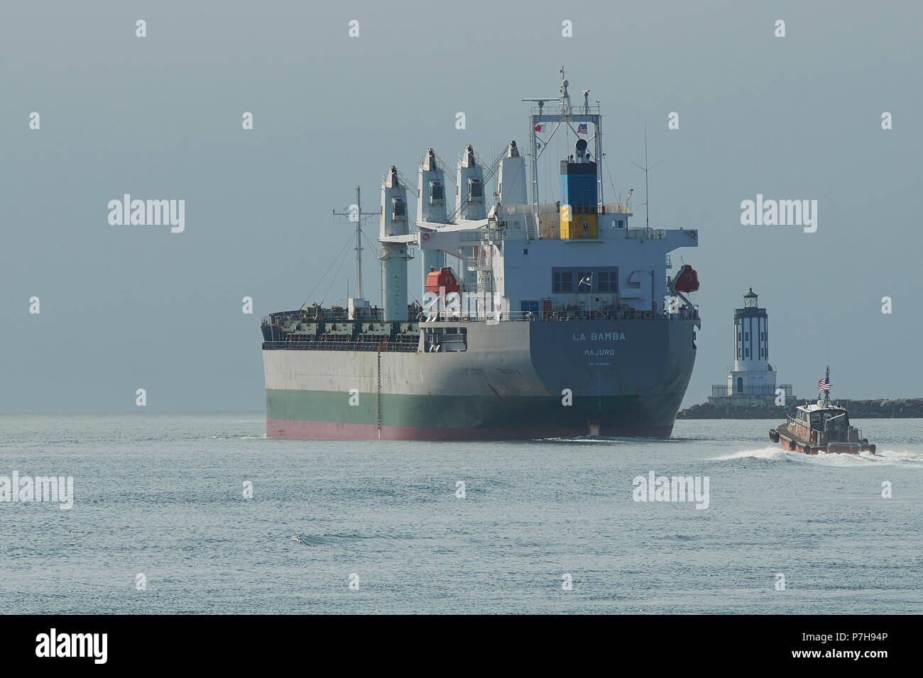 Harbor Pilot Boat Follows The Bulk Carrier, LA BAMBA, Under Way And Leaving The Port Of Los Angeles, California. The Angels Gate Lighthouse To Right. Stock Photo
