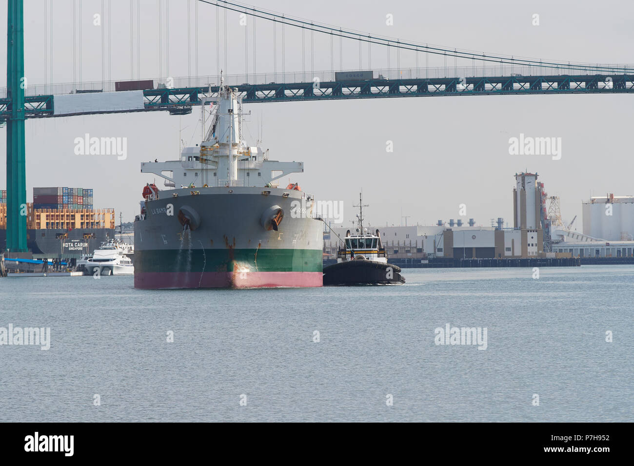 Head On View Of The Bulk Carrier, LA BAMBA, Escorted By Tugs & Leaving The Port Of Los Angeles, California. The Vincent Thomas Bridge Behind. Stock Photo