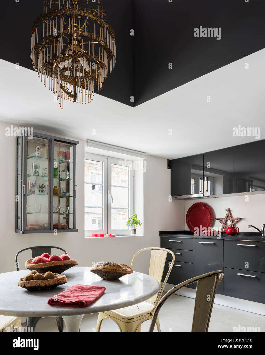 Dark grey flat fronted units in kitchen with vintage metal Tolix dining chairs and circular marble topped table Stock Photo