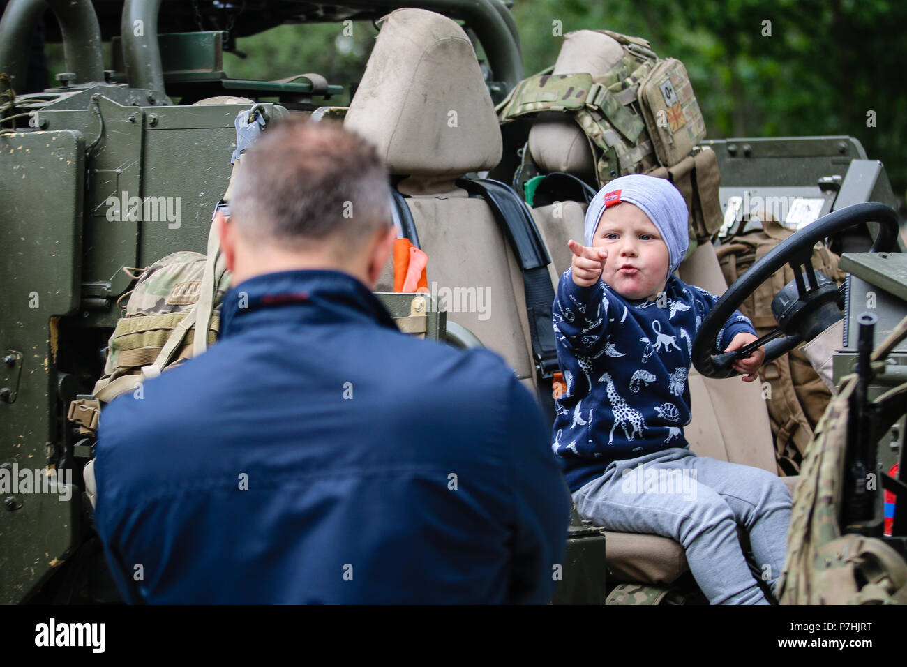 A Polish child points at his father while siting in a Mobility Weapon-Mounted Installation Kit “Jackal” with the U.K. army 1st The Queen's Dragoon Guards during a static display with Battle Group Poland at Giżycko, Poland on June 30, 2018. Battle Group Poland is a unique, multinational coalition of U.S., U.K., Croatian and Romanian Soldiers who serve with the Polish 15th Mechanized Brigade as a deterrence force in support of NATO’s Enhanced Forward Presence. (U.S. Army photo by Spc. Hubert D. Delany III /22nd Mobile Public Affairs Detachment) Stock Photo