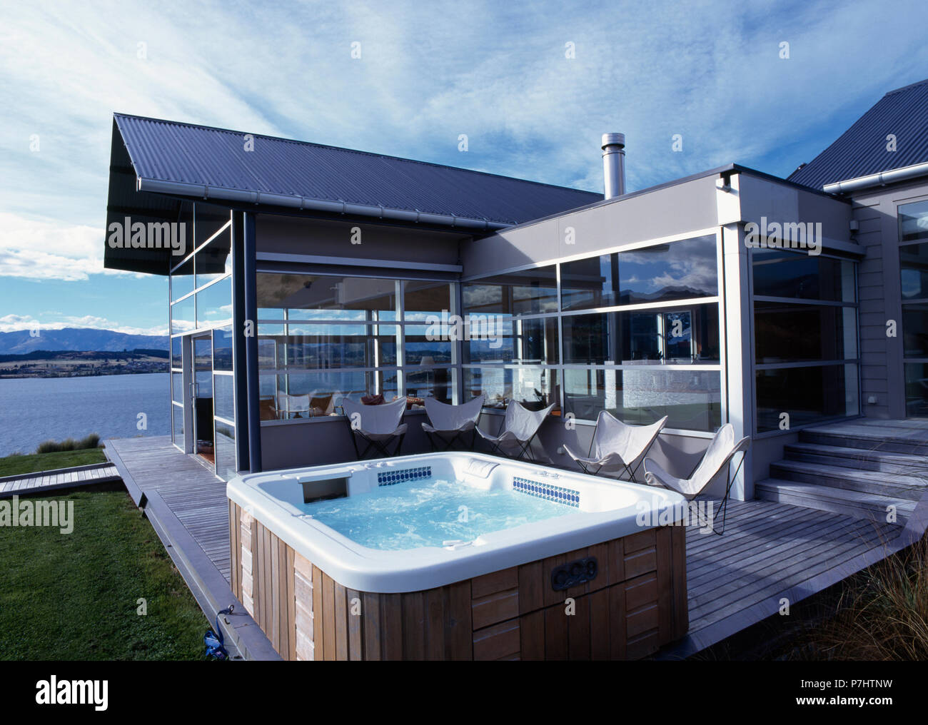 Butterfly chairs and hot tub on decking outside modern architectural house beside the ocean in New Zealand Stock Photo