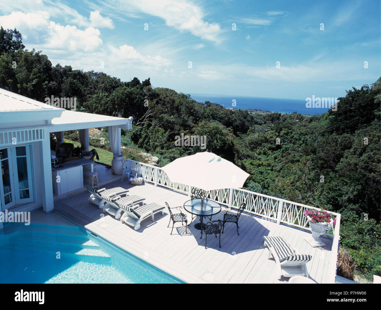 Loungers and umbrella beside swimming pool and hillside house in Barbados Stock Photo