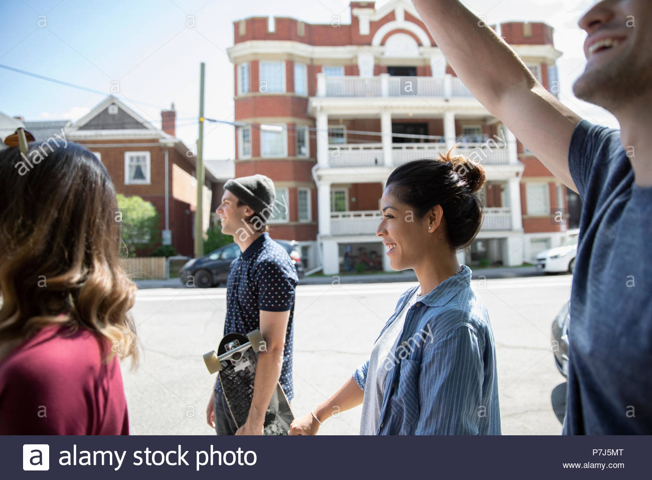 Millennial friends walking on sunny neighborhood sidewalk Stock Photo