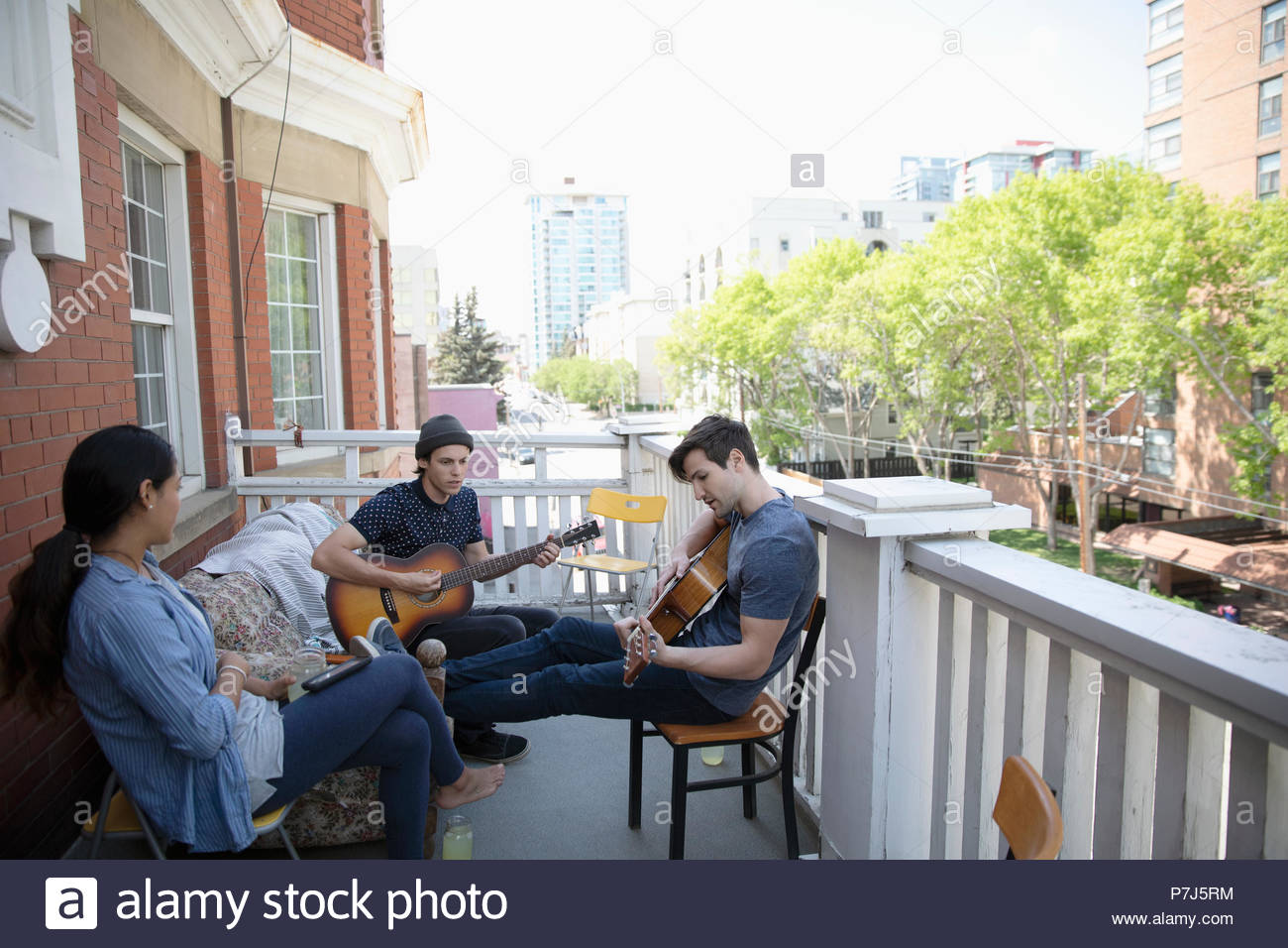 Millennial friends hanging out, playing guitars on apartment balcony