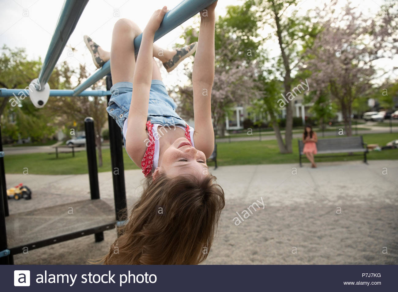 Playful girl hanging upside down from monkey bars at playground Stock Photo...