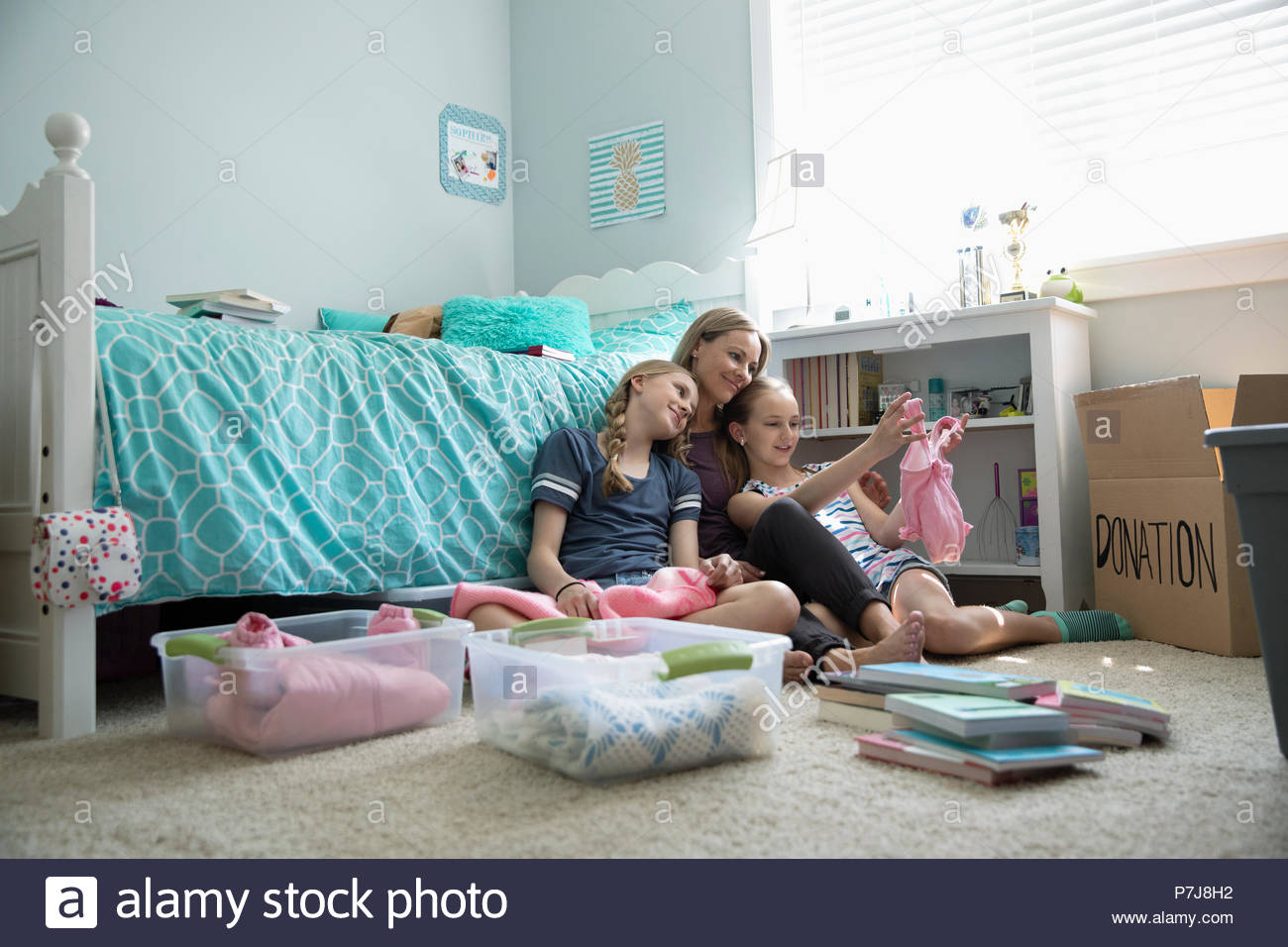 Mother and daughters donating baby clothes in bedroom Stock Photo