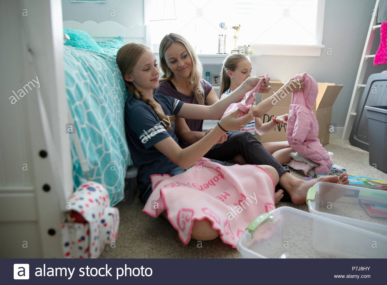 Mother And Daughters Donating Baby Clothes In Bedroom Stock Photo