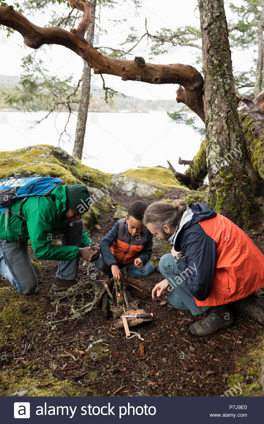 Trail guide teaching father and son how to build campfire in woods Stock Photo