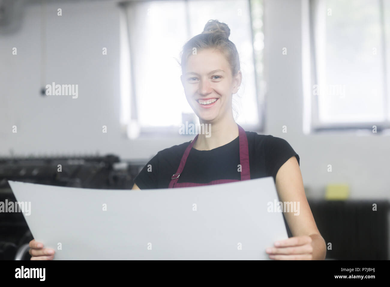 Smiling Woman standing by a printing press holding a piece of paper Stock Photo