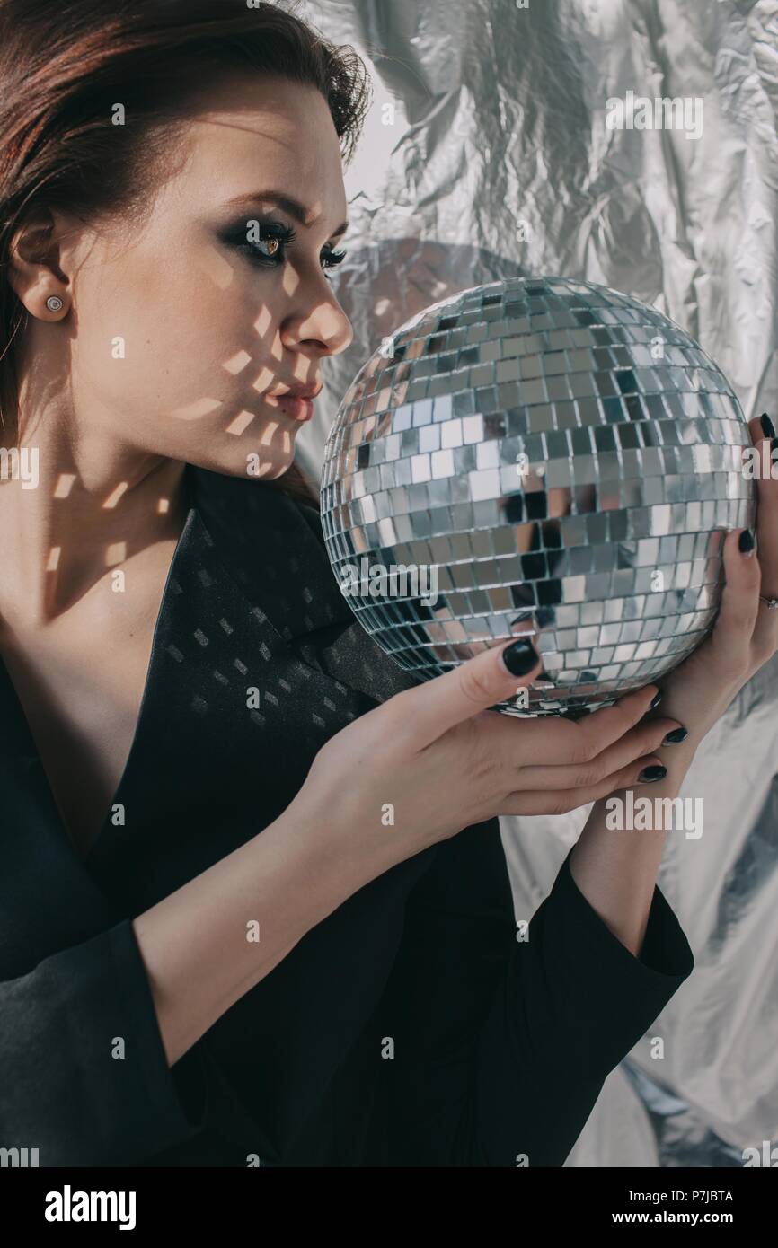 Portrait of a woman looking into the reflection of a silver disco ball Stock Photo