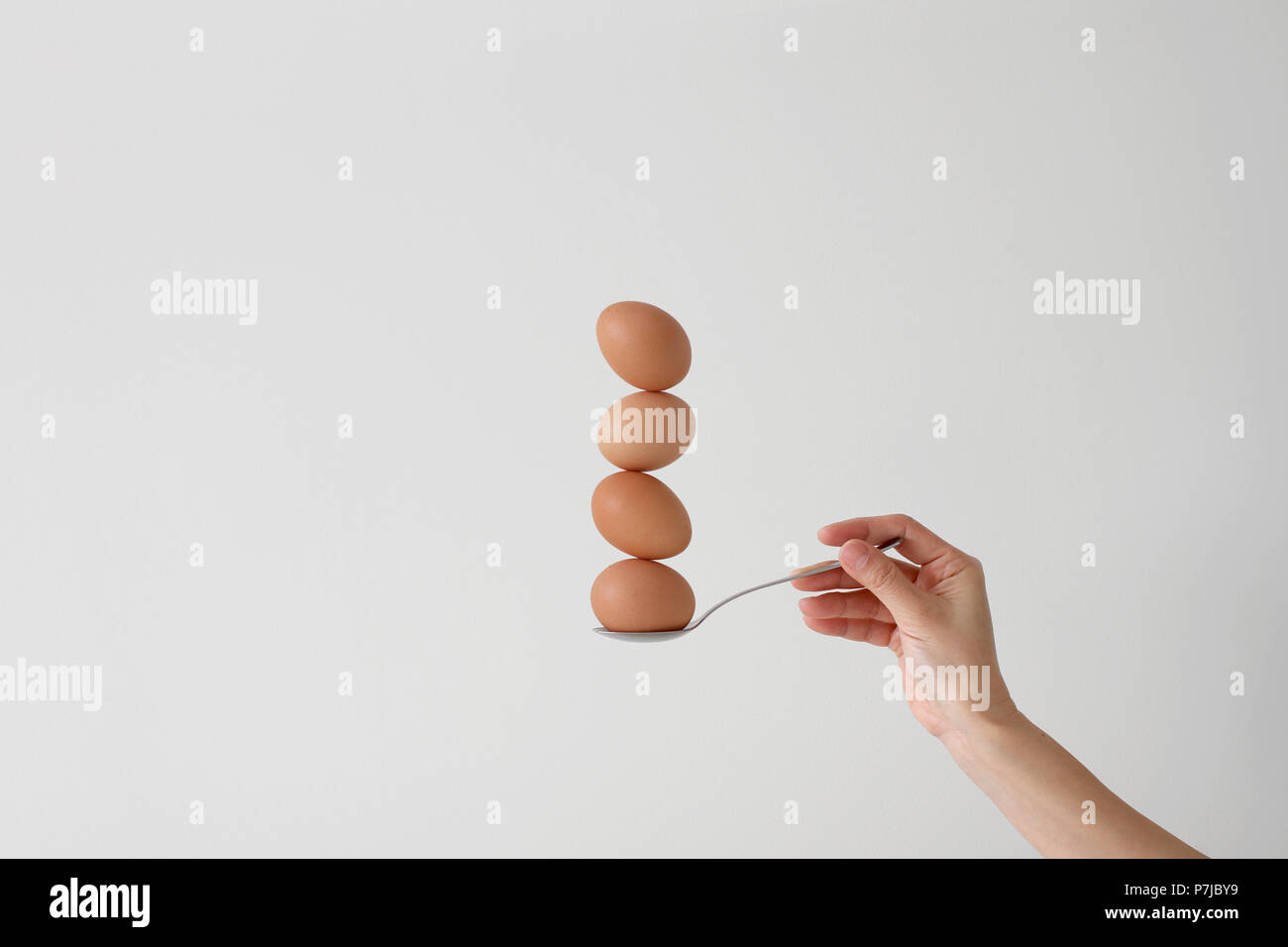 Woman's hand holding a spoon with four eggs balancing on top of each other Stock Photo