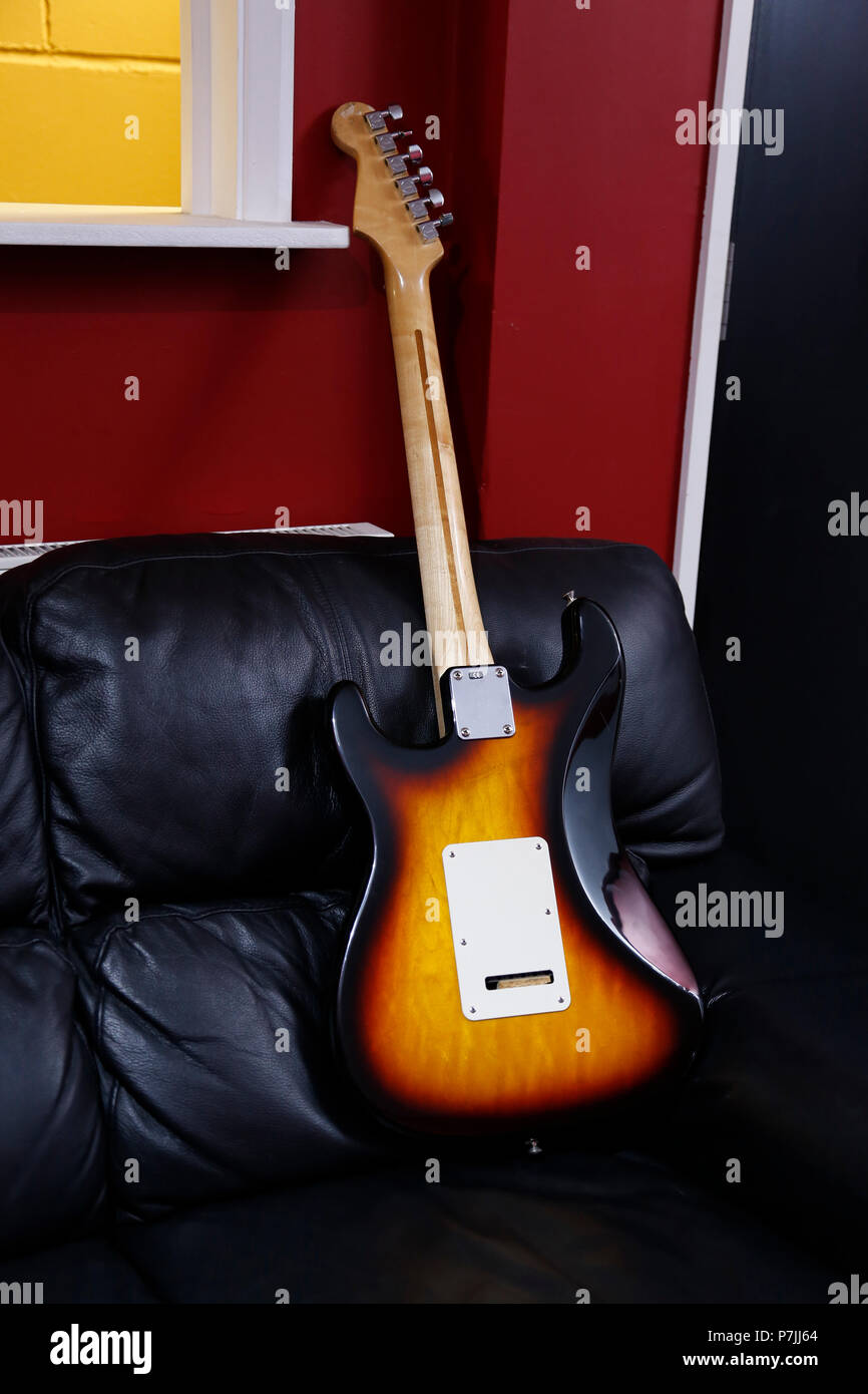 Guitar leaning on black leather sofa Stock Photo