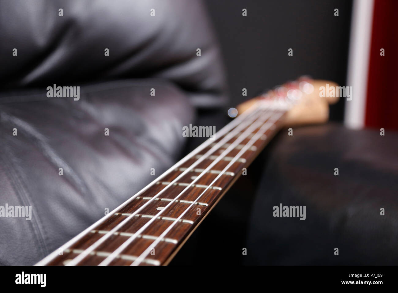 Bass guitar neck lying on black sofa Stock Photo
