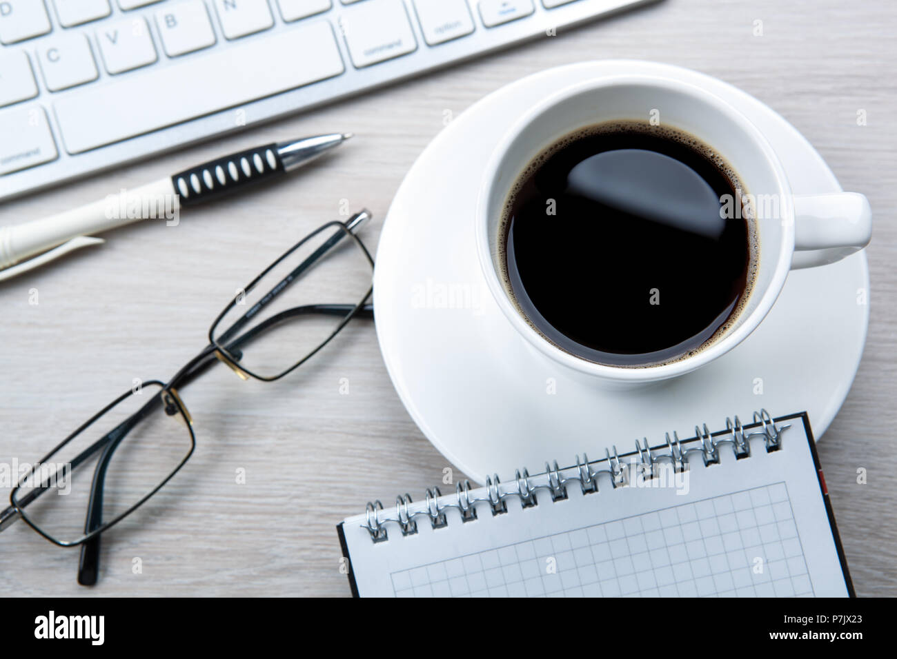white cup of black coffee, glasses, keyboard on the desktop Stock Photo