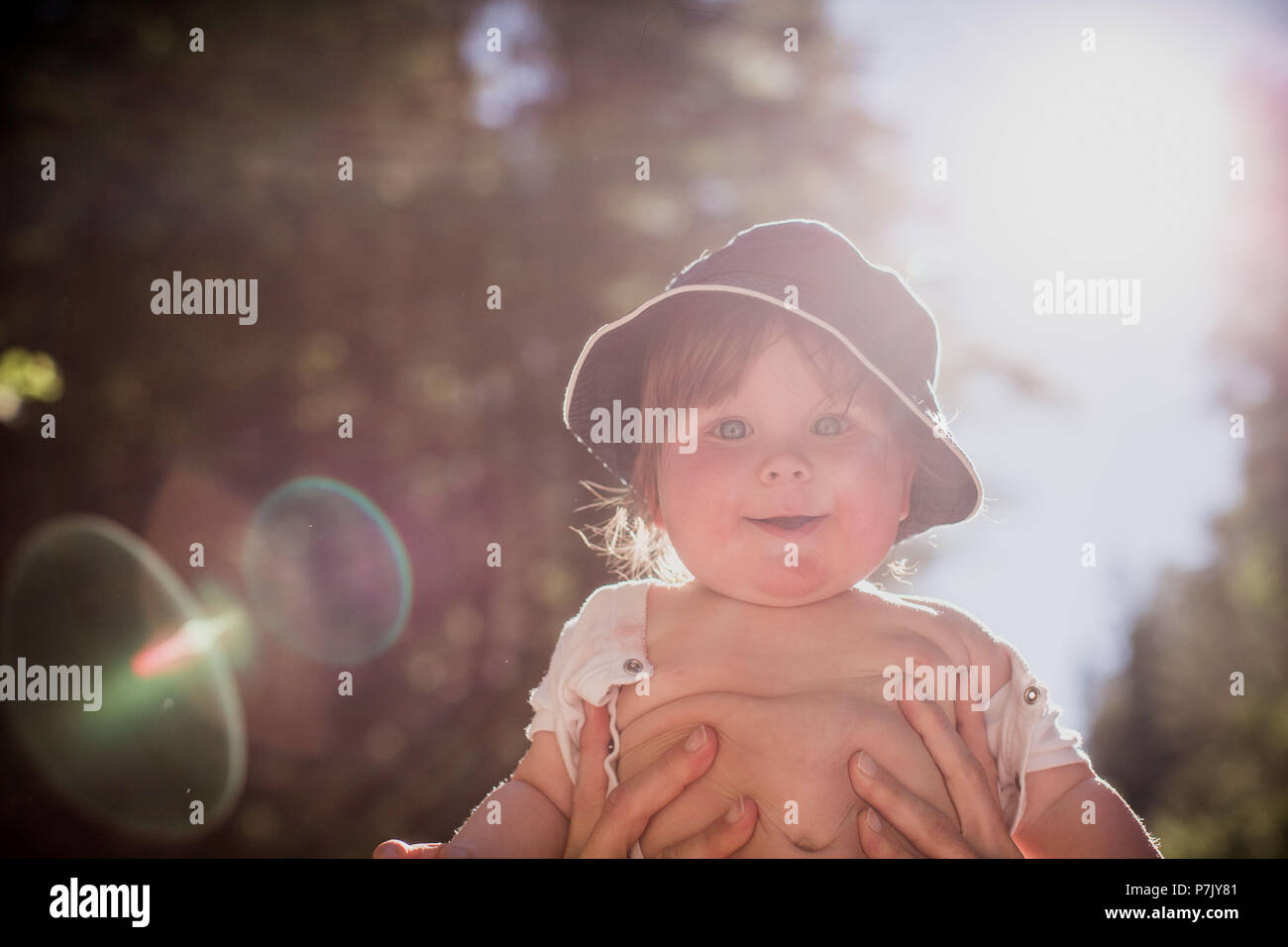 held up toddler, smiling, looking into camera, backlight, Stock Photo