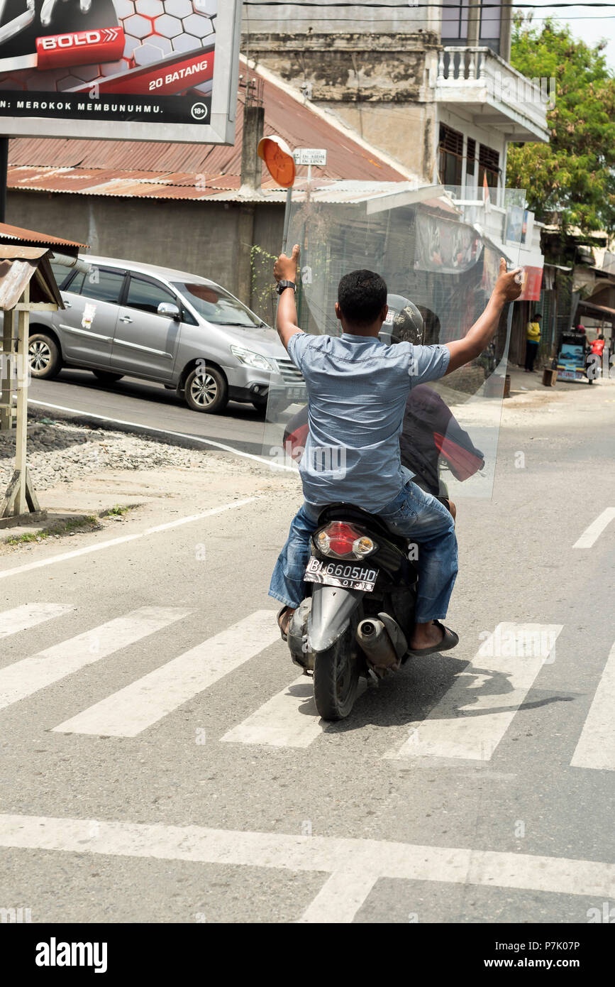 Two men carrying a glass pane on a moped, Stock Photo