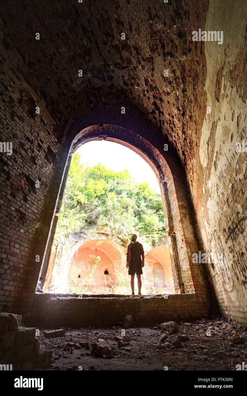 tourist standing in arch of weathered dark corridor of old fortress Stock Photo