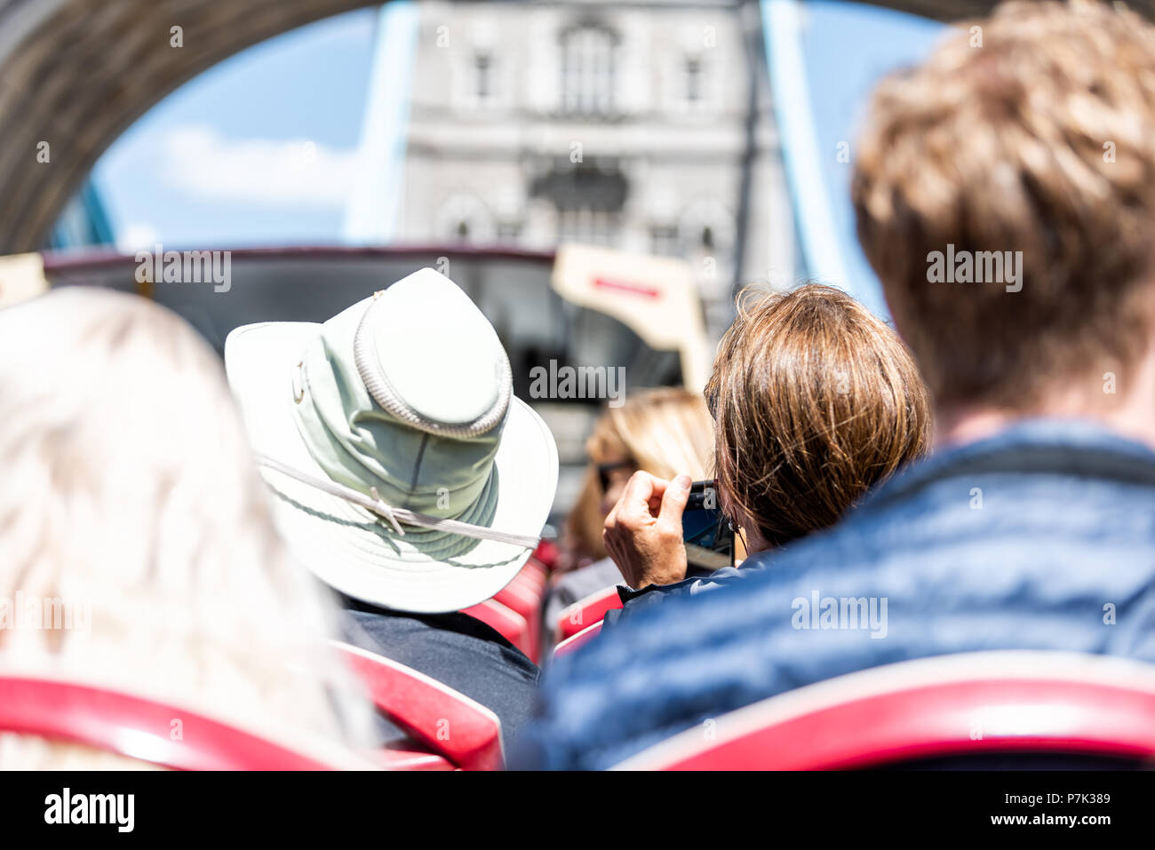 London, UK - June 22, 2018: Back of people tourists sitting in seats, looking at view of city tower bridge on street road double decker red big bus in Stock Photo