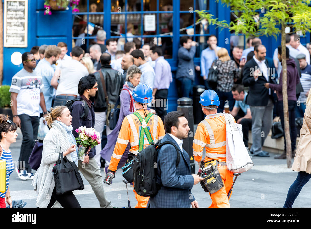 London, UK - June 22, 2018: Crowd of many people two construction workers pedestrians walking by London Bridge street road in center of downtown city, Stock Photo