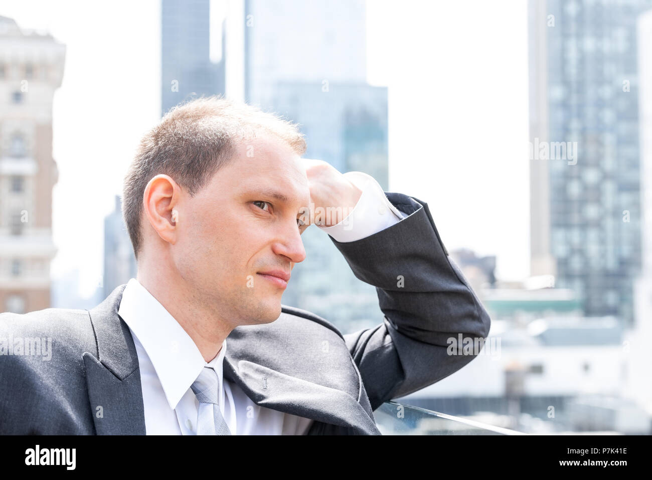 Handsome, attractive young side profile businessman closeup face portrait standing in suit, tie, looking at New York City cityscape skyline in Manhatt Stock Photo