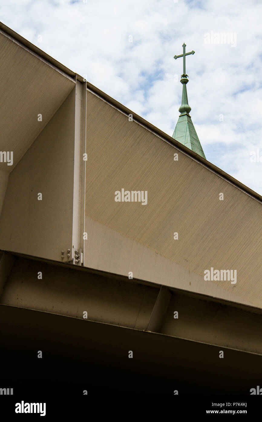 Catholic cross on top of a green roof church behind metallic structure