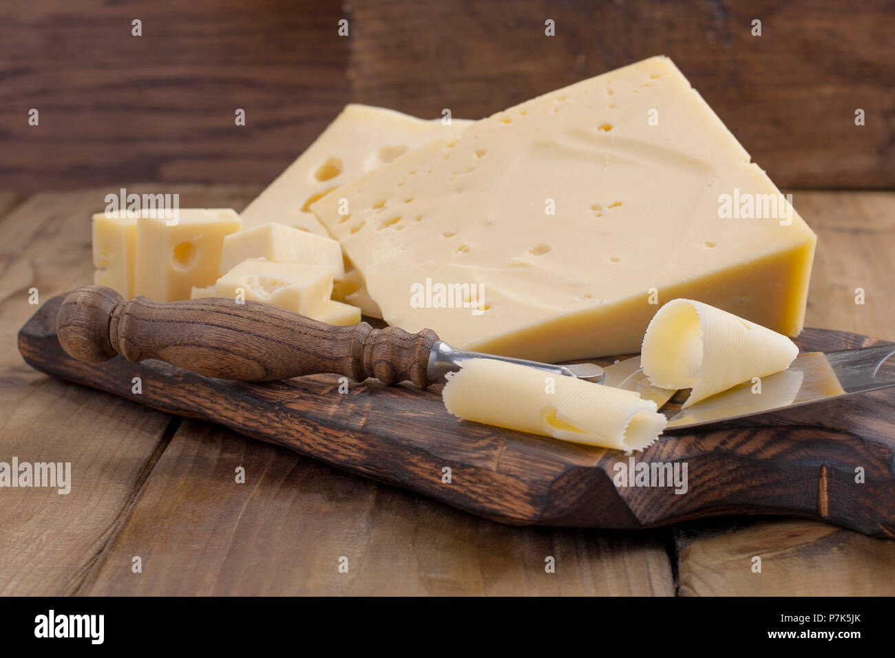 Cheese with holes large and small. Wooden board and knife. Traditional