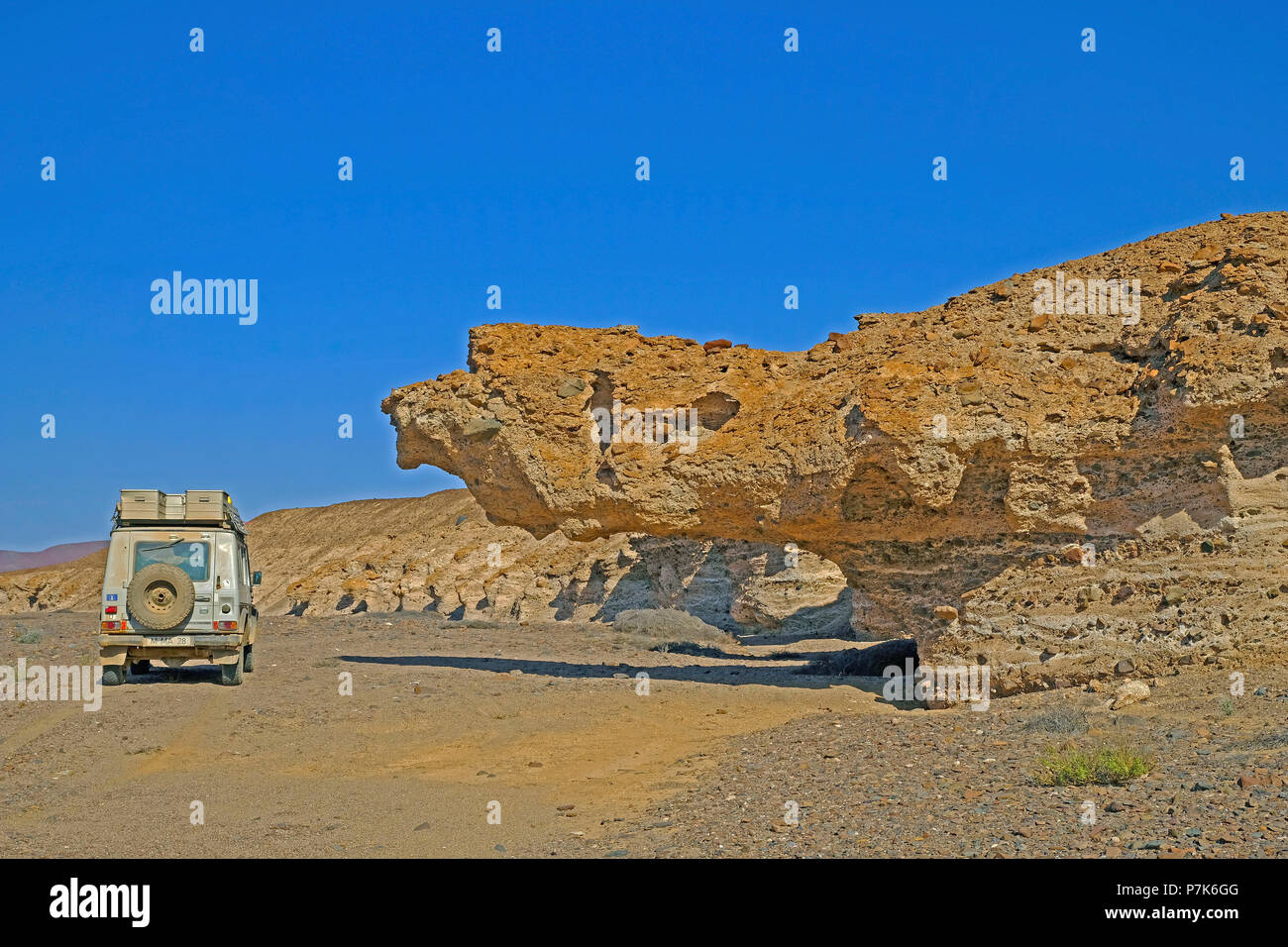 under-washed, overhanging terraces and steep bank with coloured inclusions on a tributary of the dry river Messum with off-road vehicle in the Dorob National Park in Namibia Stock Photo