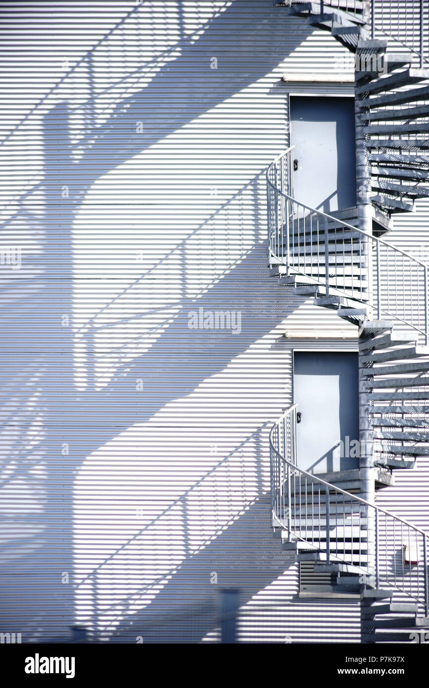 Spiral staircase / fire escape on the side facade of an industrial building casts a shadow, Stock Photo