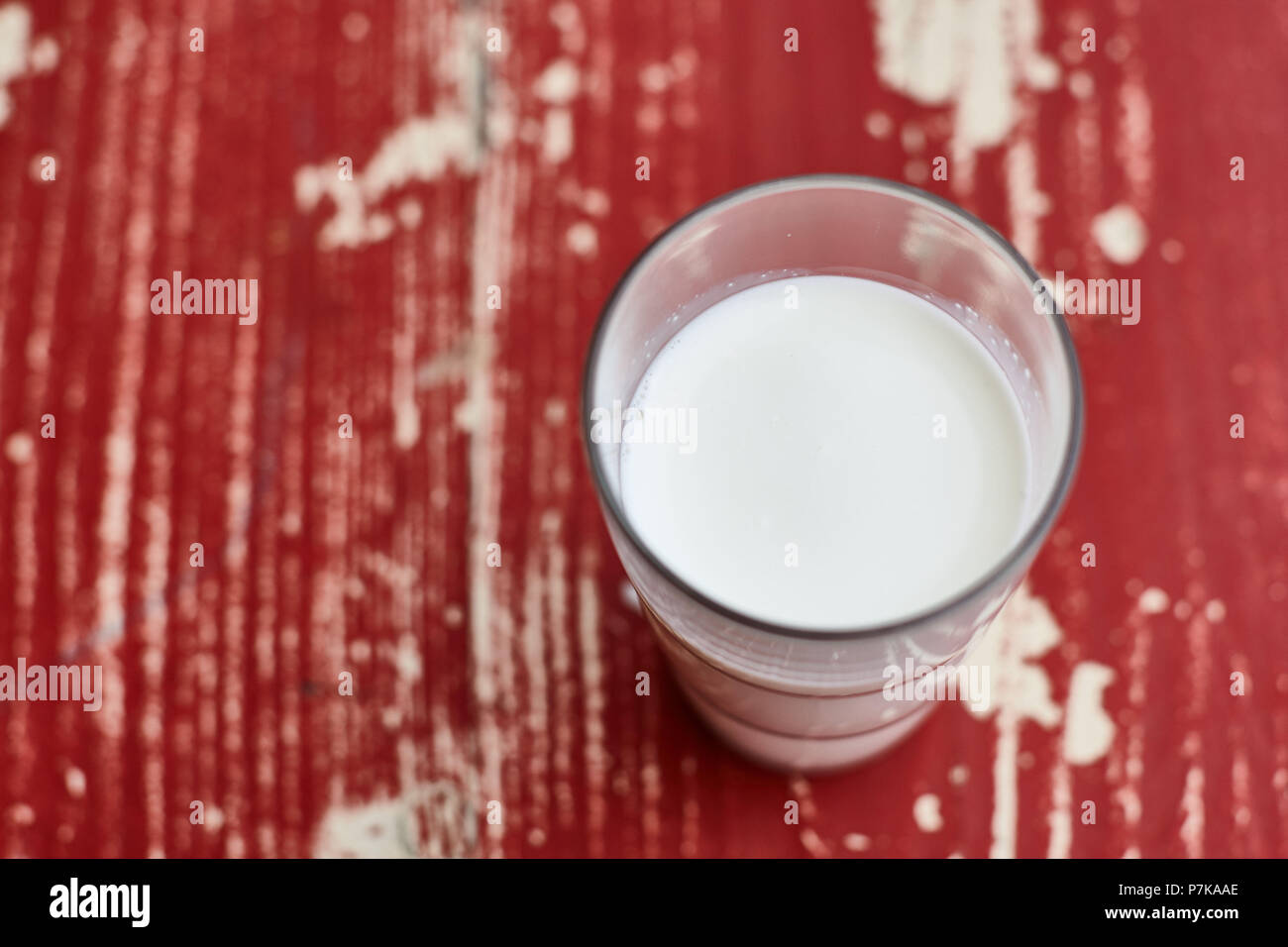 Glass of milk on red wooden table, full glass, from above Stock Photo