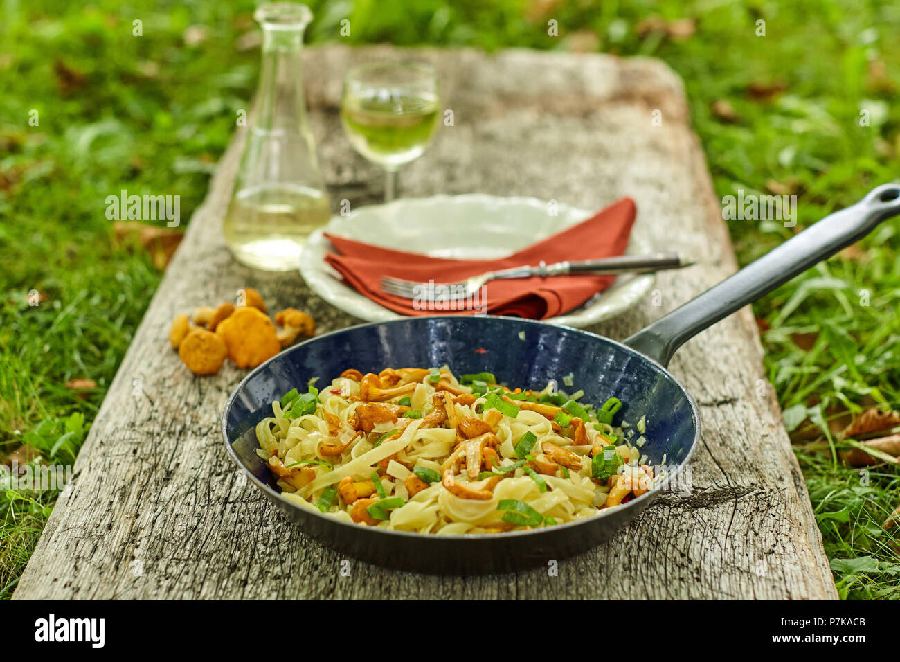 Pan with tagliatelle and chanterelles with place setting and wine on old wooden board Stock Photo