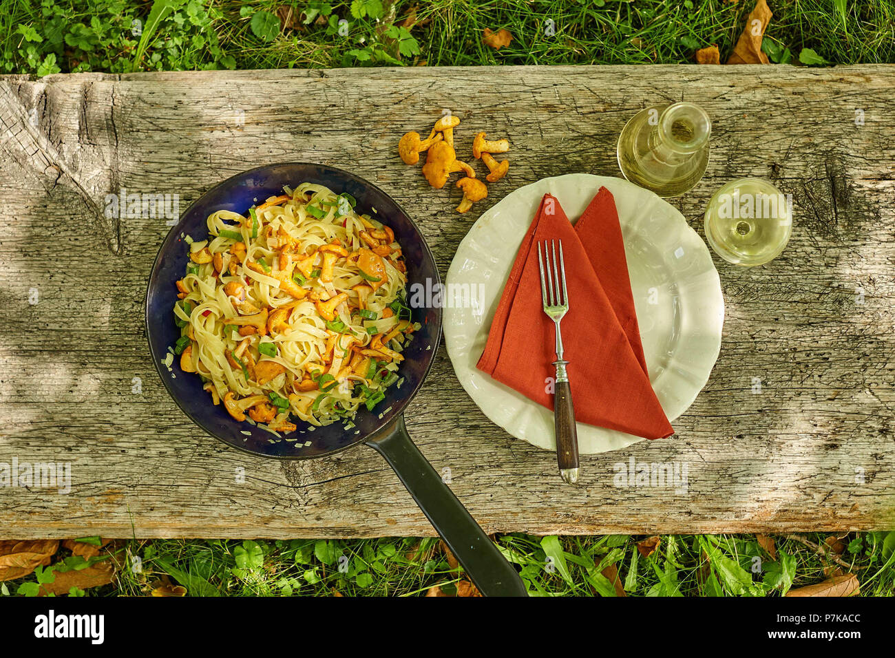 Pan with tagliatelle and chanterelles with place setting and wine on old wooden board Stock Photo