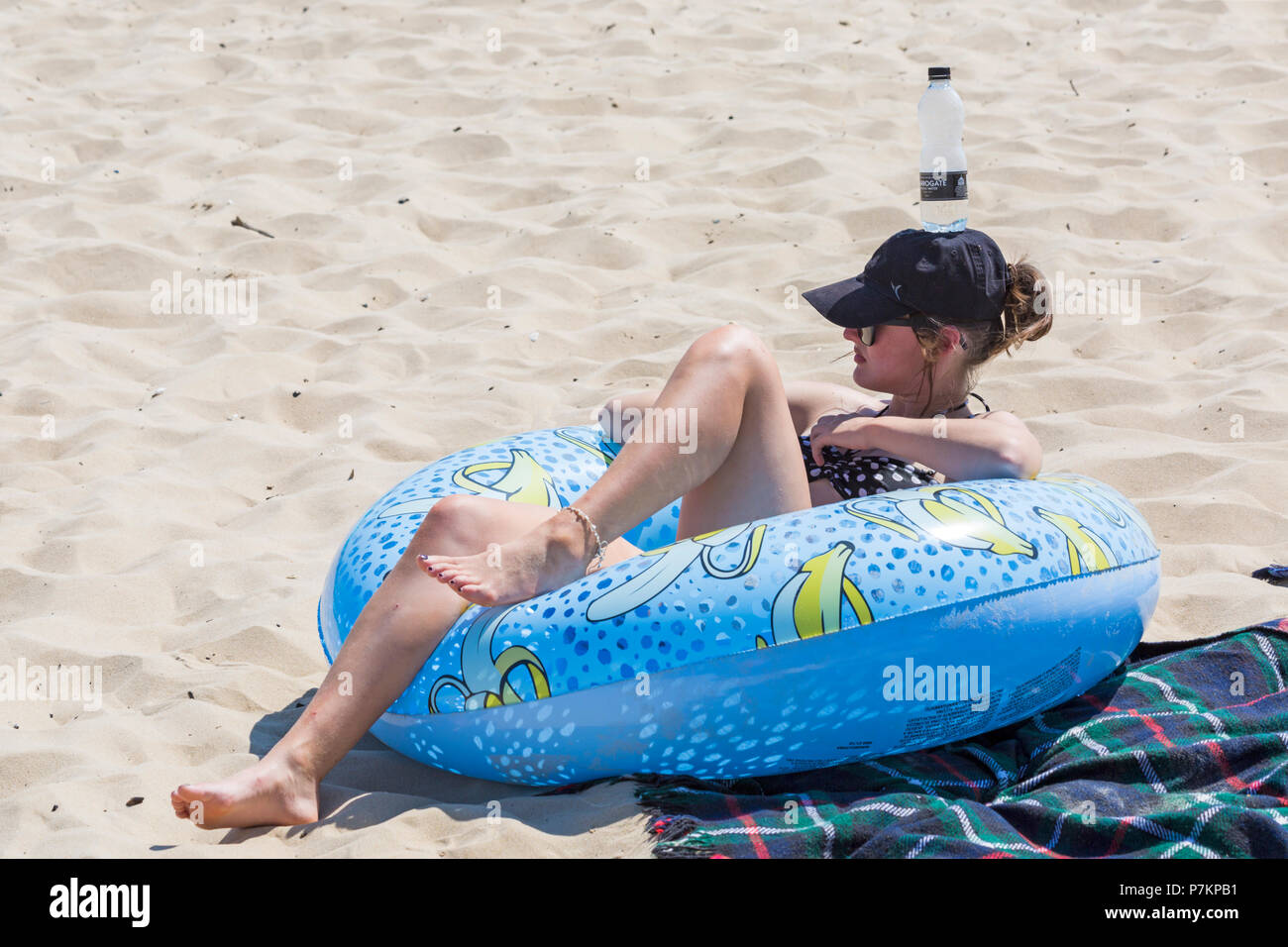 Bournemouth, Dorset, UK. 7th July 2018. UK weather: another hot sunny day as the heatwave continues and thousands of sunseekers head to the seaside with temperatures rising to enjoy the sandy beaches at Bournemouth on the South Coast even with the big match on! Keeping a bottle of water handy! Young woman relaxing sunbathing in inflatable ring donut with bottle of water on her head. Credit: Carolyn Jenkins/Alamy Live News Credit: Carolyn Jenkins/Alamy Live News Credit: Carolyn Jenkins/Alamy Live News Stock Photo