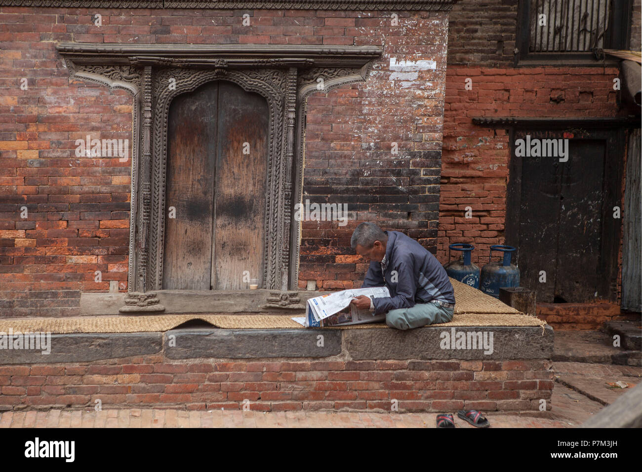 Local man reading newspaper in front of old house, Kathmandu, Nepal Stock Photo