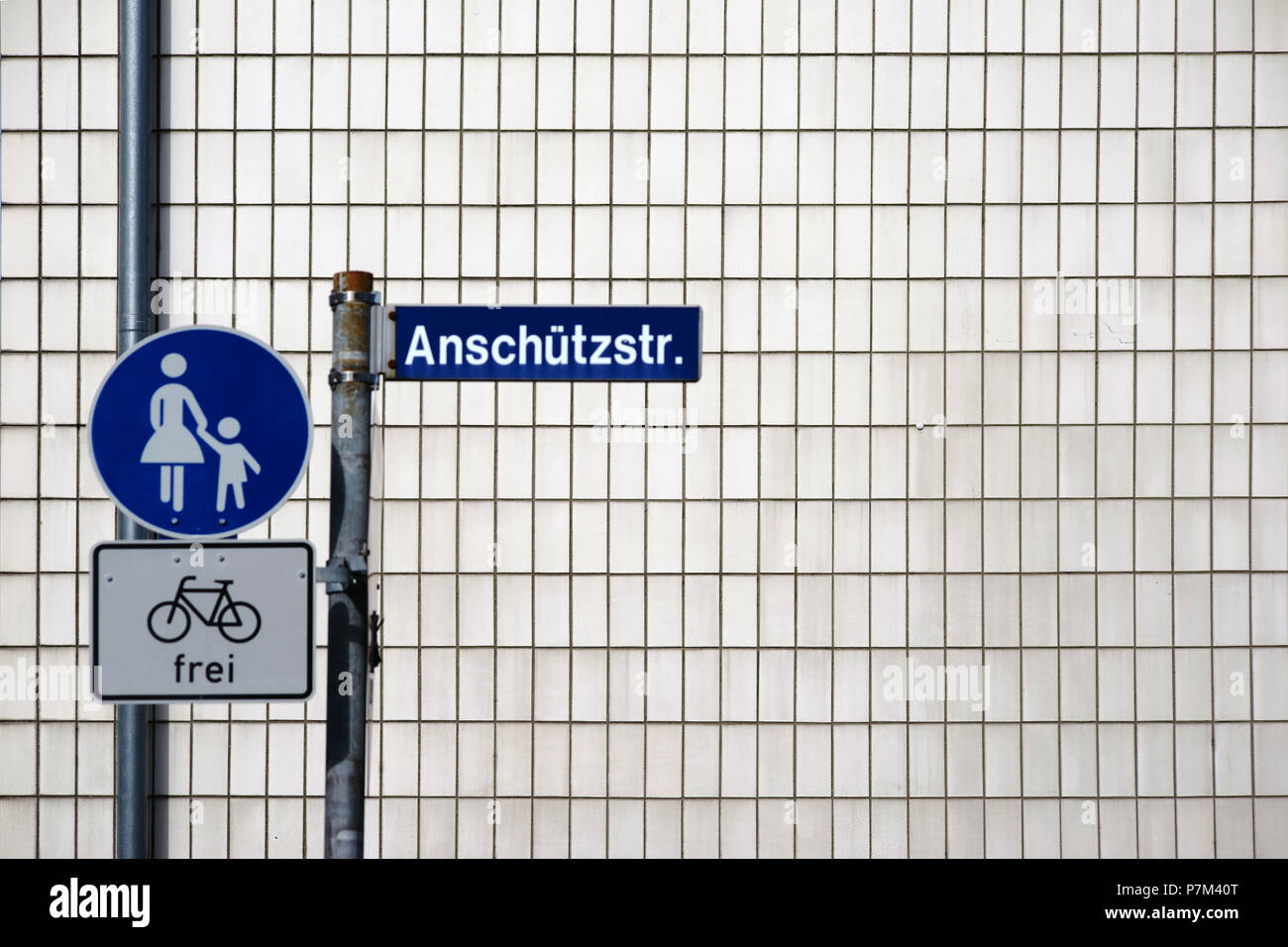 A vertical street nameplate and pedestrian crossing sign on the corner of a residential building with brick facade. Stock Photo