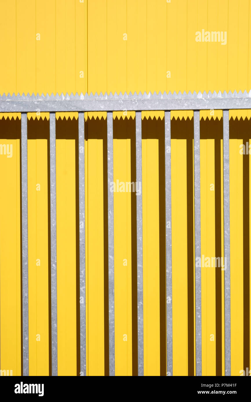 Side view of a color intensive corrugated iron wall of a shopping mall with a lanky pointed-ragged part of an open driveway gate. Stock Photo