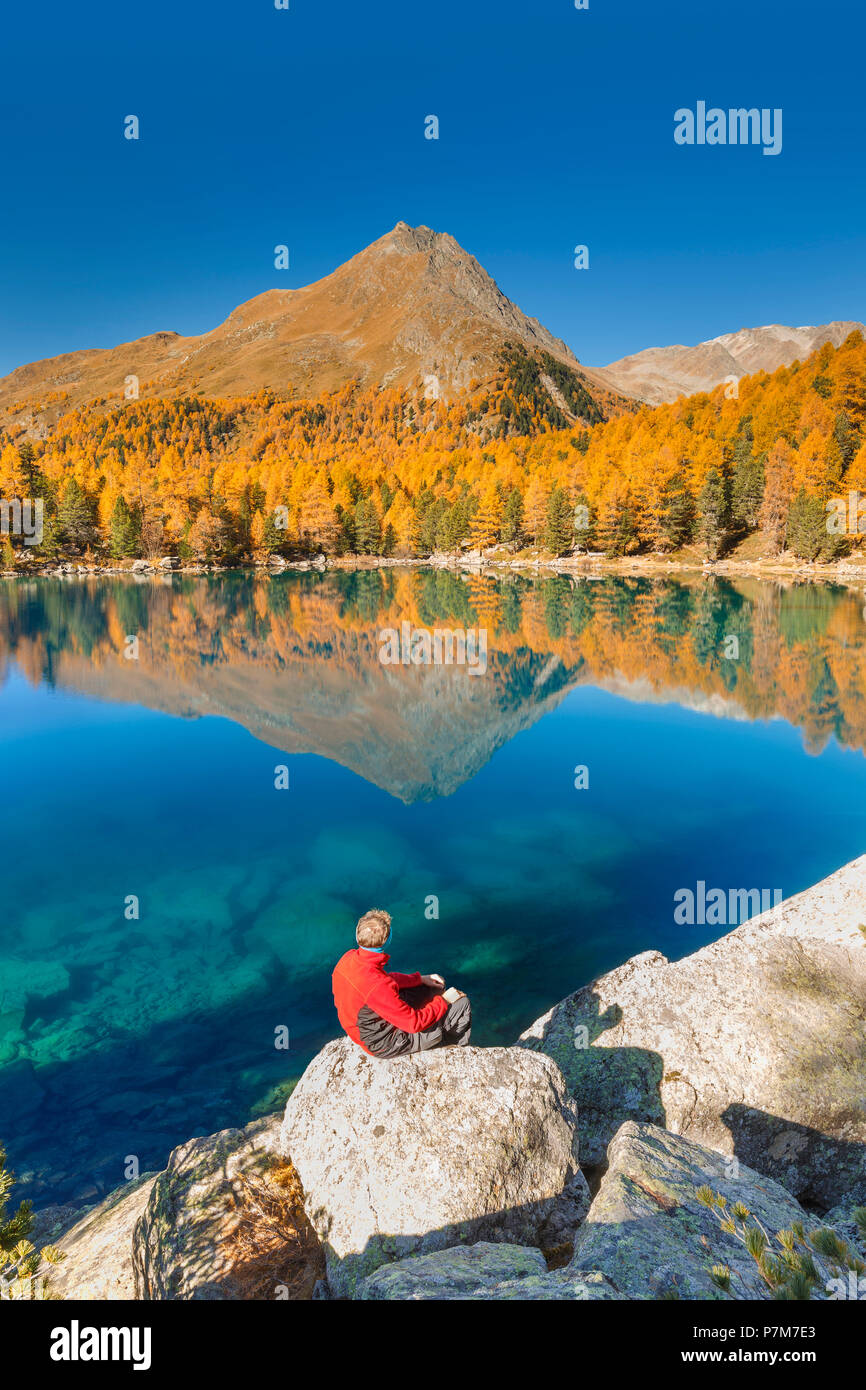 Hiker take a break to admire lake Saoseo in a perfect autumn day, Poschiavo, val di Campo, Canton of Graubunden, Switzerland, Europe Stock Photo