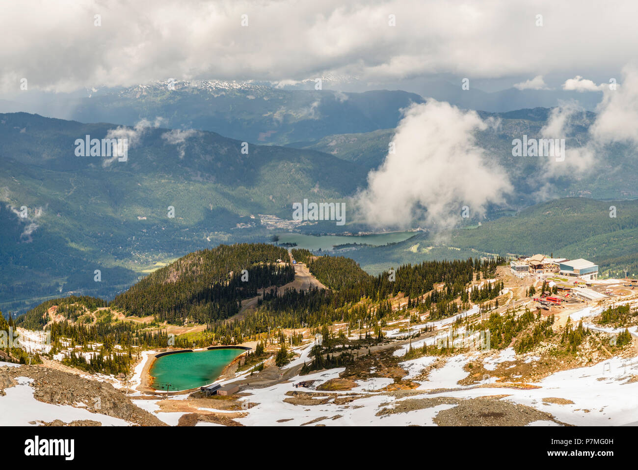 Top view of mountains covered with forests and snow, lakes and roads, white fluffy clouds, buildings of a ski, tourist resort Stock Photo