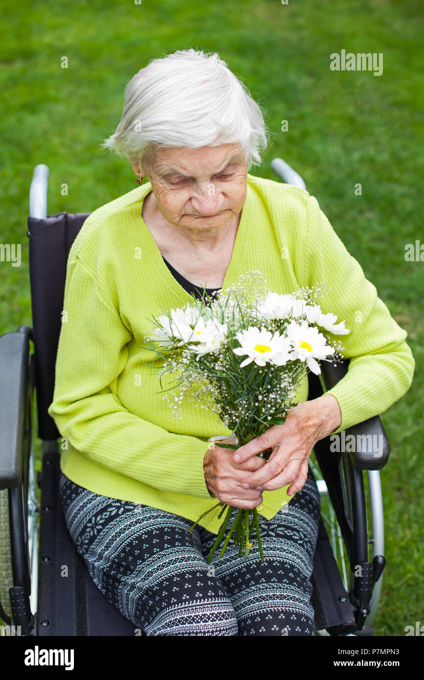 Disabled elderly woman sitting in wheelchair, receiving a flower