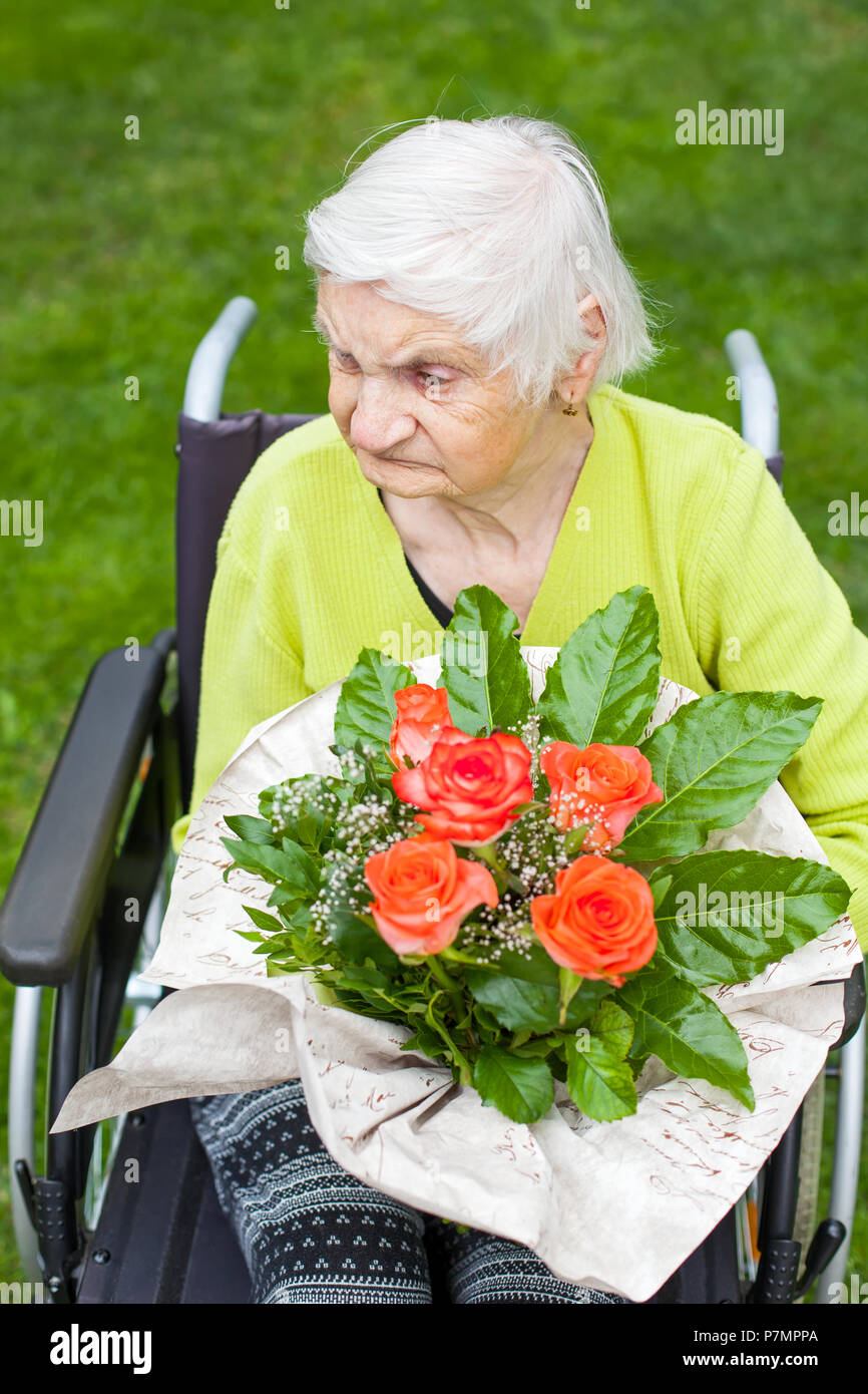 Disabled elderly woman sitting in wheelchair, receiving a flower