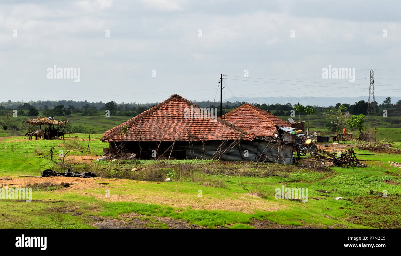 Make Shift Kutcha house with pyramid shape roof for rain water flow, in a very green landscape of indian village with mountains in background Stock Photo