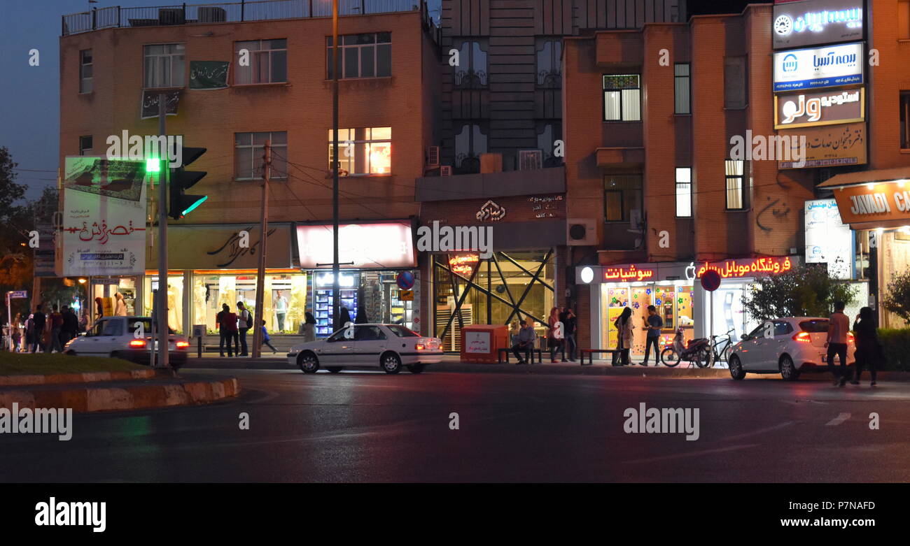 Nightlife in Iran: Iranian people meet in the streets at dusk in front of restaurant facades lit up by fluorescent and LED lights in Qazvin, Iran Stock Photo